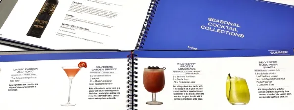 Open cocktail recipe books with visible pages showing drink names, ingredient lists, and images of four different cocktails under the heading "Seasonal Cocktail Collections.