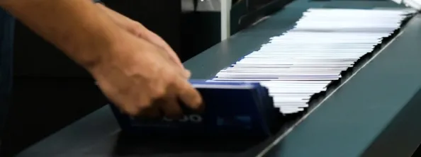 A person’s hands organize a stack of envelopes on a conveyor belt, suggesting a process of sorting or handling mail.