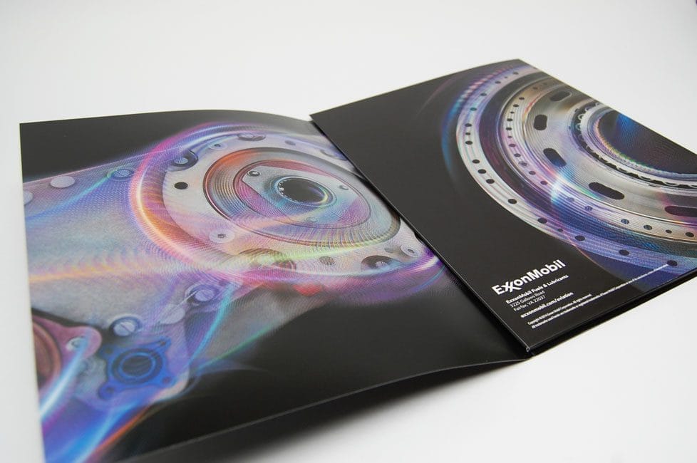 Open glossy brochure showing close-up of colorful mechanical gear artwork on black pages; includes small white text logo in corner (brand not fully legible).